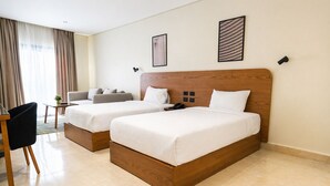 A hotel room with two beds, a desk, a chair, and a sofa. - NewCity Hotel & Suites (New Cairo)
