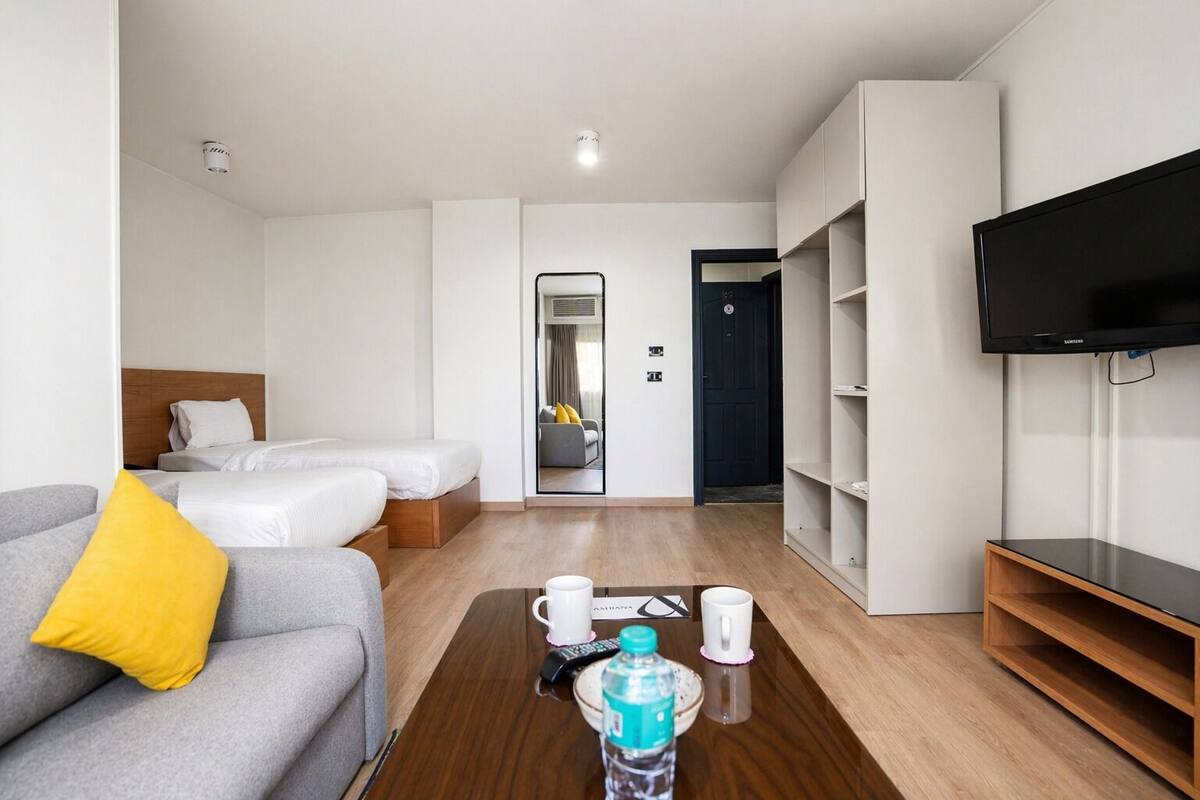 A hotel room with a sofa, two beds, a TV, a coffee table with cups and a bottle, and a mirror.