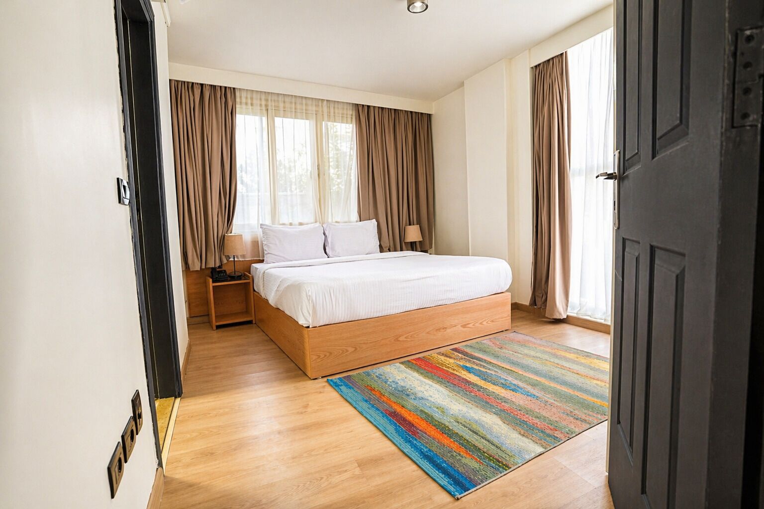 A bedroom with a wooden bed, a colorful rug, and a window with curtains.