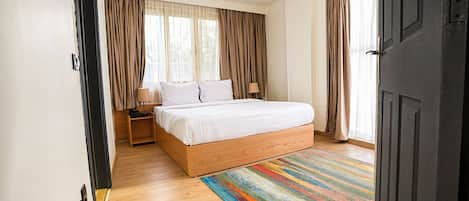 A bedroom with a wooden bed, a colorful rug, and a window with curtains.