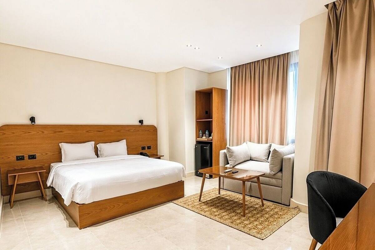 A hotel room with a wooden bed, a sofa, a desk, and a television.