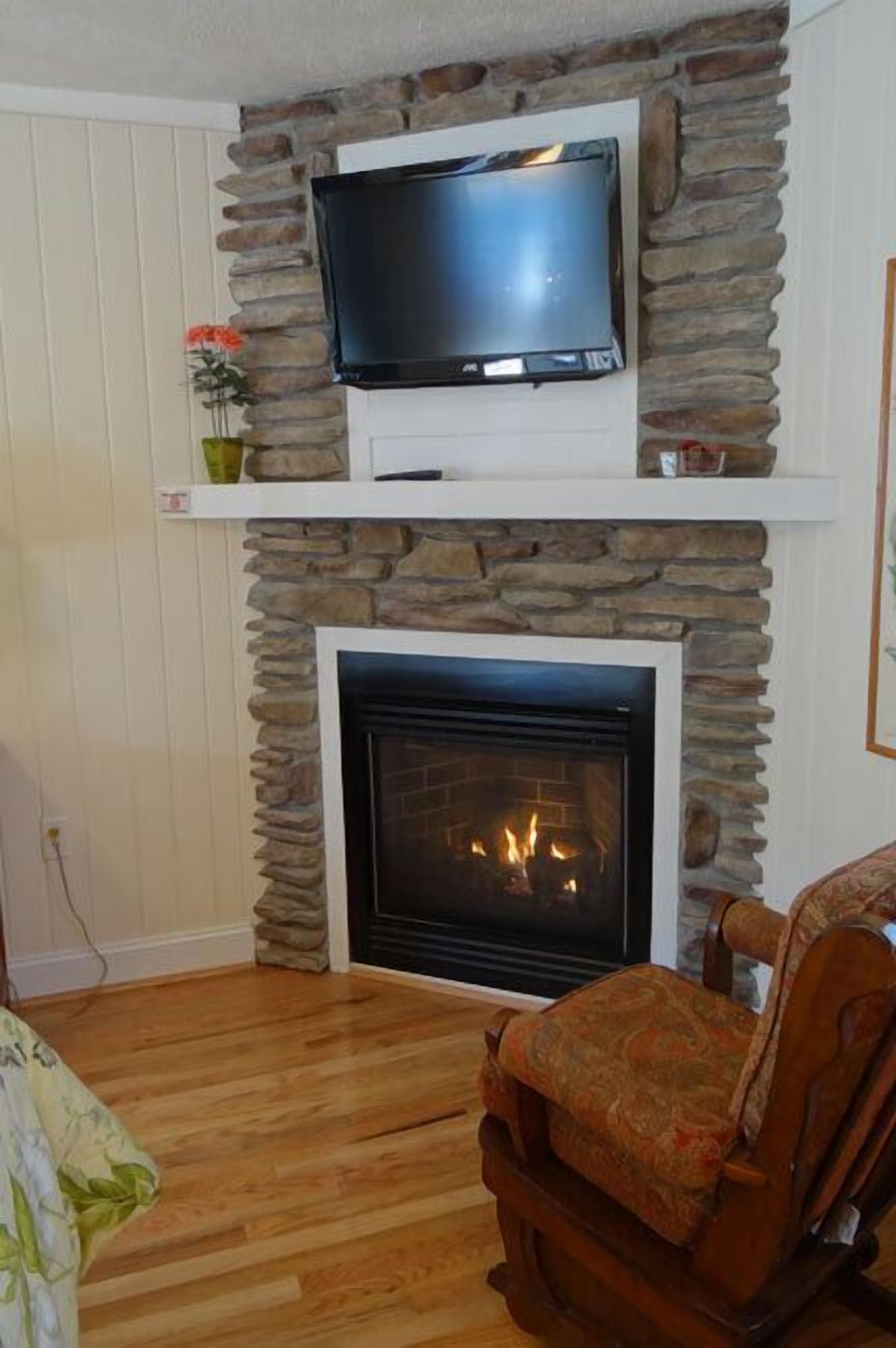 A living room with a stone fireplace, a mounted television, and a wooden floor.