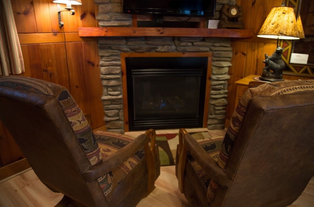 Un salon chaleureux avec une cheminée en pierre, des fauteuils en cuir et un téléviseur placé au-dessus.