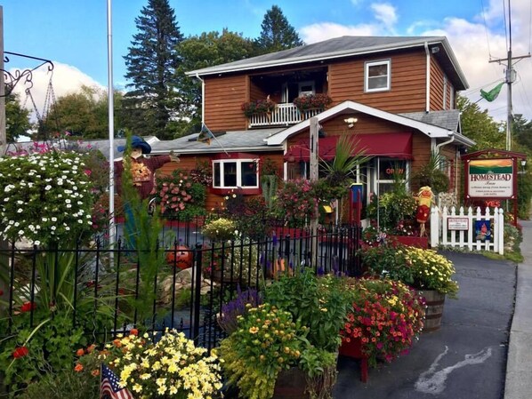 Una casa de madera con porche, rodeada de diversas flores y plantas.