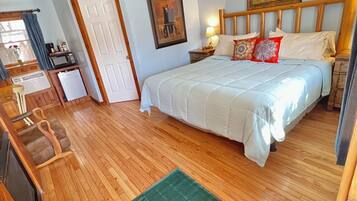 A bedroom with a bed, wooden floor, ceiling fan, and a green rug.
