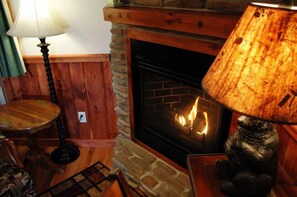 A cozy room with a stone fireplace, a table, and a lamp.