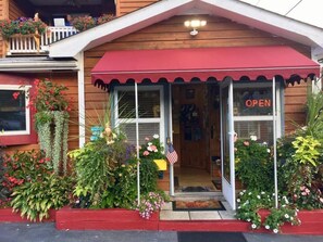 A wooden building with a red awning, a small porch with a white railing, and a door with an 'OPEN' sign.