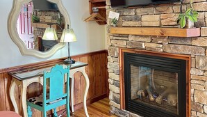 A living room with a stone fireplace, a flat-screen TV, a wooden desk, and a teal chair.