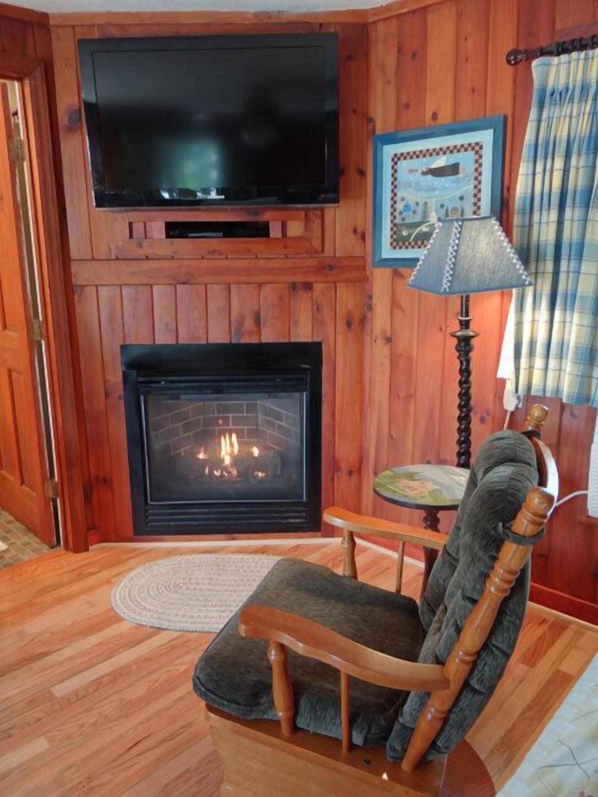 Ein gemütliches Zimmer mit Kamin, einem darüber angebrachten Fernseher und einem Holzstuhl.