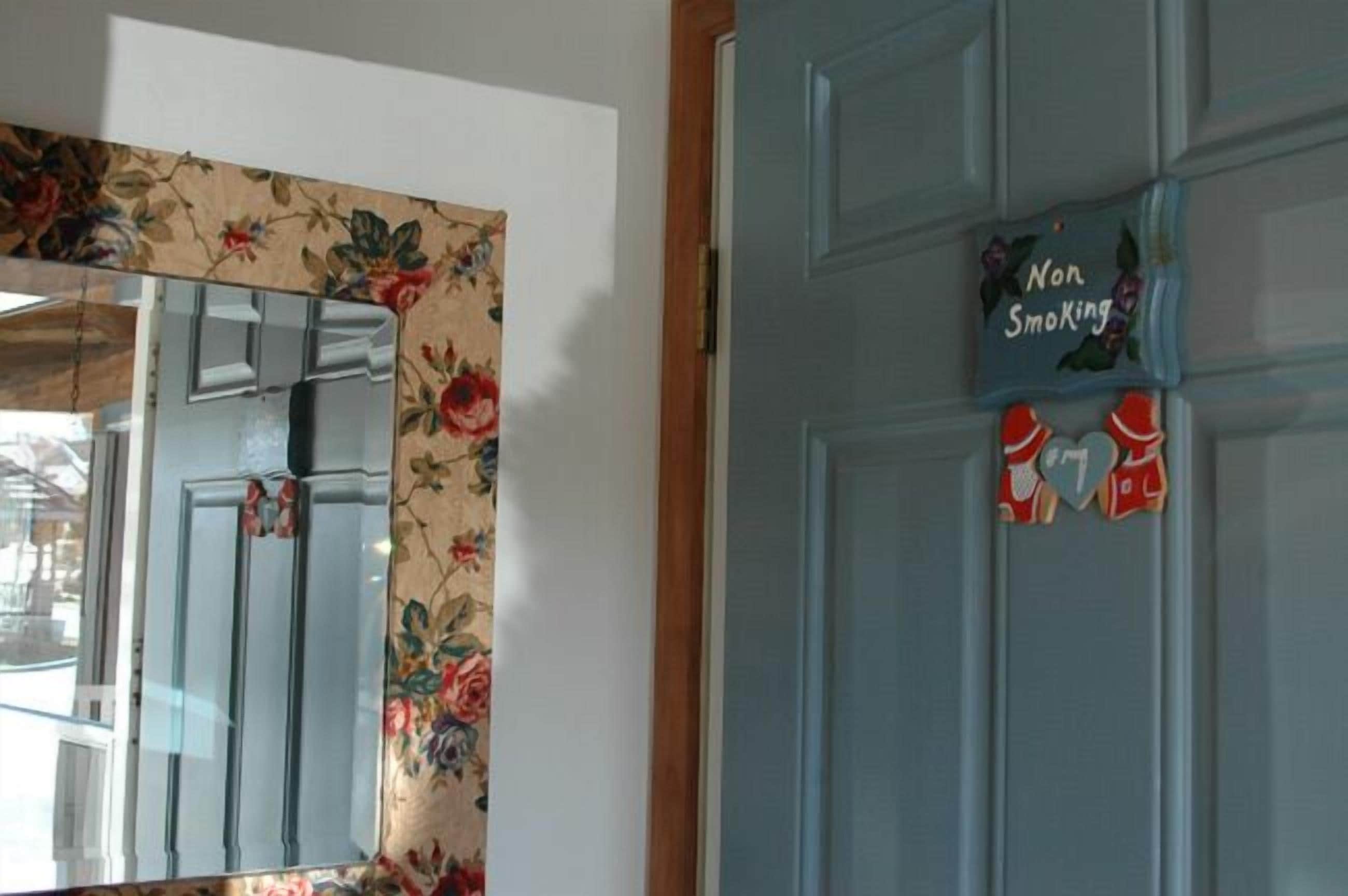 A room with a floral wallpaper, a blue door with a 'Non Smoking' sign, and a mirror reflecting part of the room.