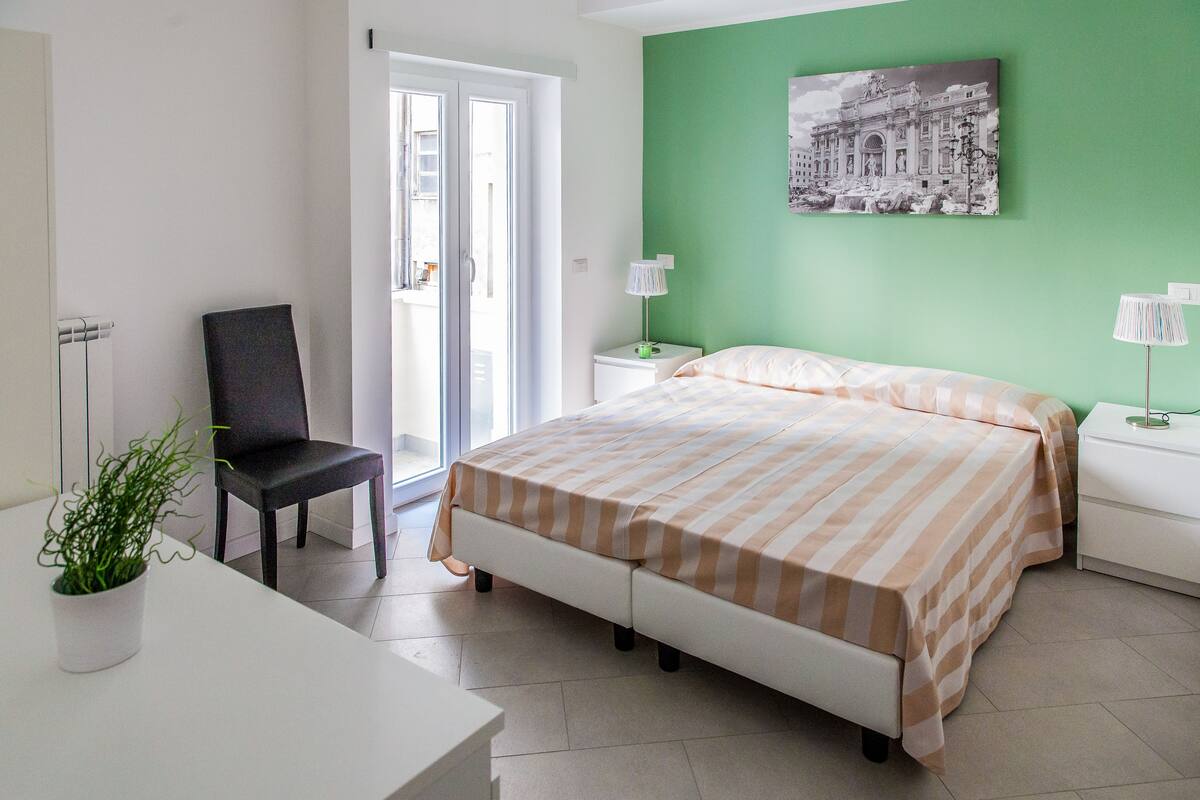 A bedroom with a bed, a chair, a desk, and a potted plant.