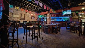 Una zona de bar con mesas y sillas de madera, pared de piedra y coloridos adornos de papel.