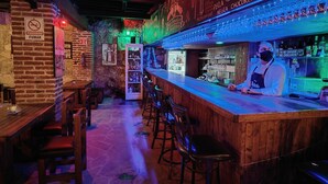 Un bar con una barra larga, taburetes y un letrero de neón.