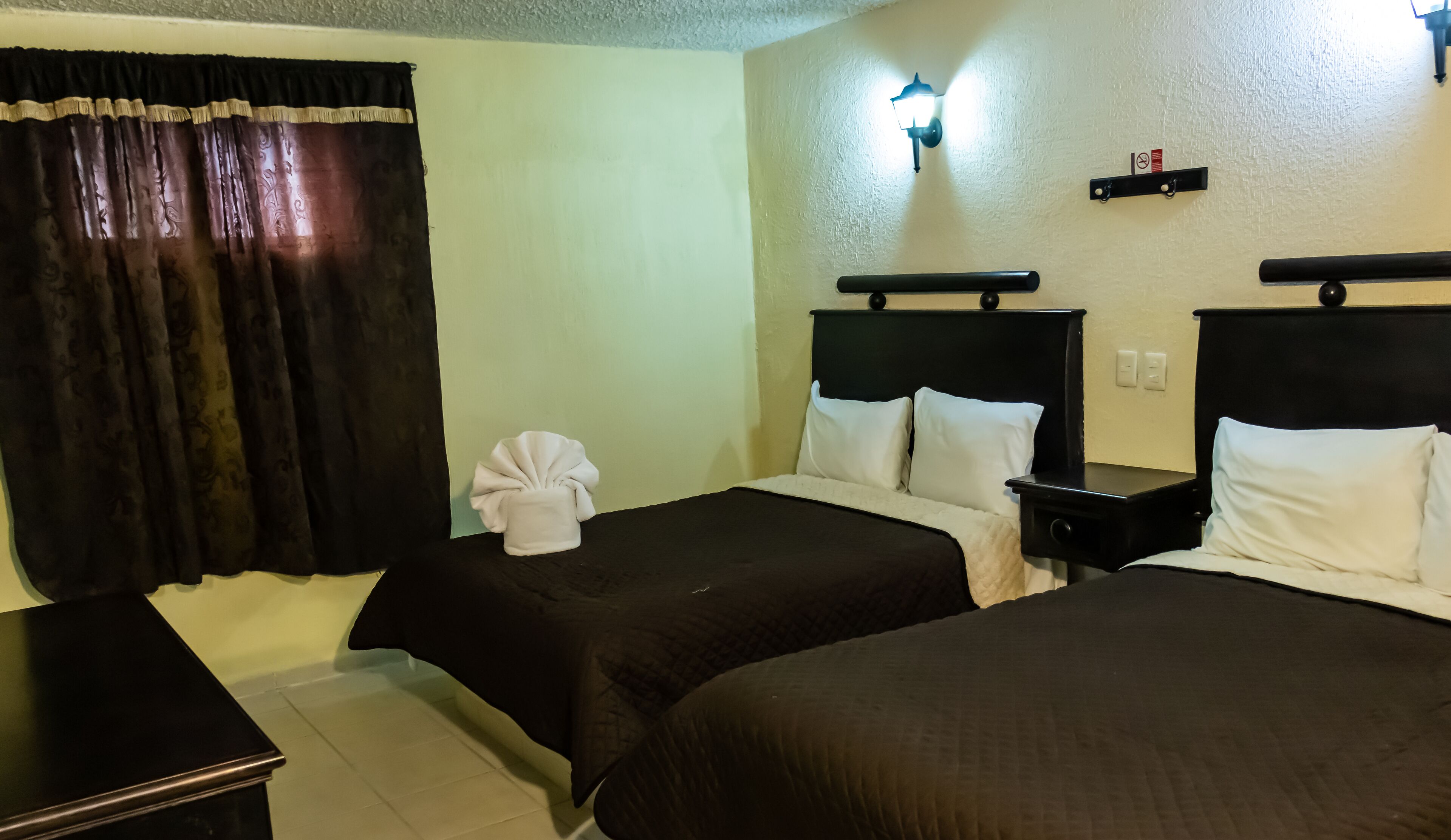 A hotel room with two beds, a nightstand, a lamp, and a curtain.