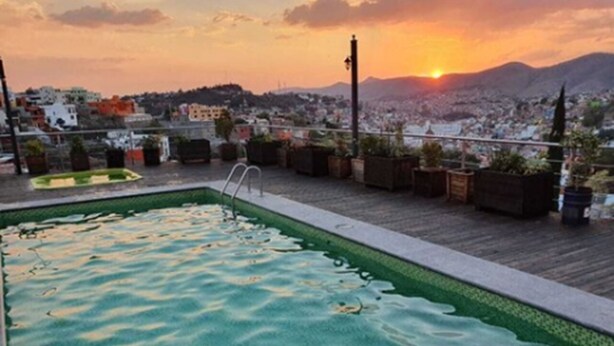 Una piscina en la azotea con vistas a un paisaje urbano y montañas al atardecer.