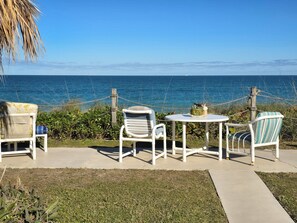 Un patio frente al mar con sillas y una mesa blancos, con vista al océano.