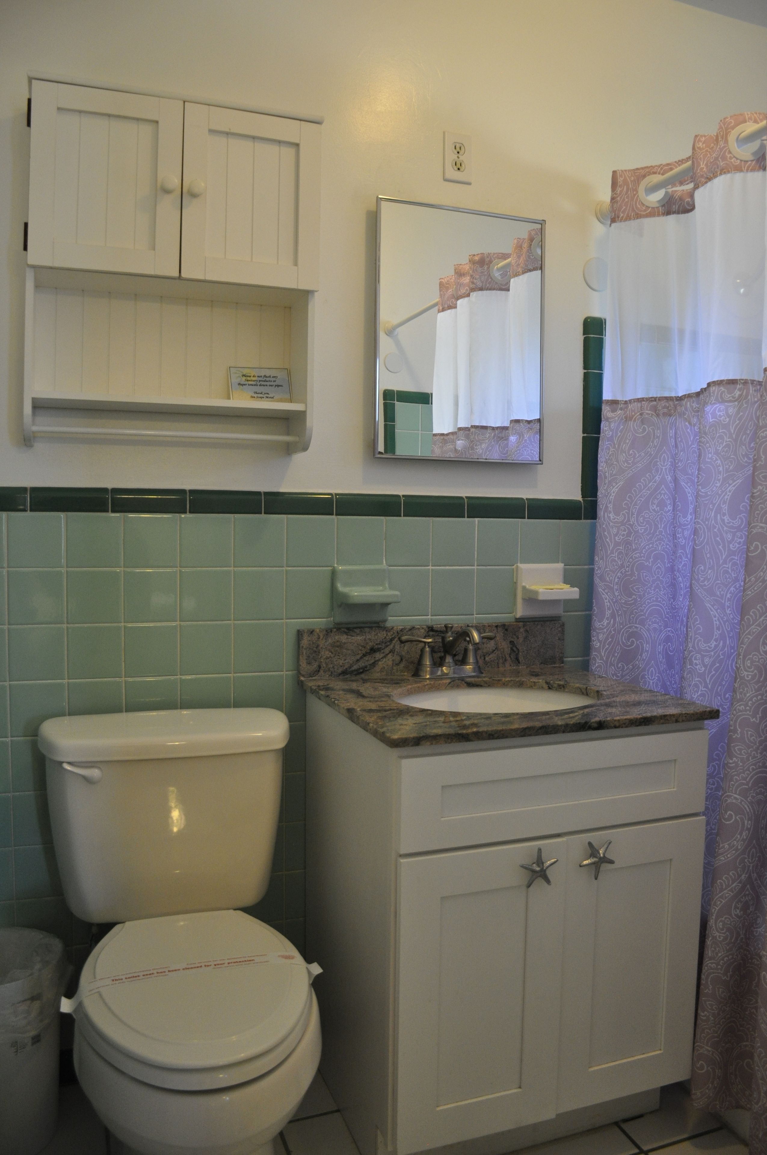 A bathroom with a toilet, sink, cabinet, and mirror.