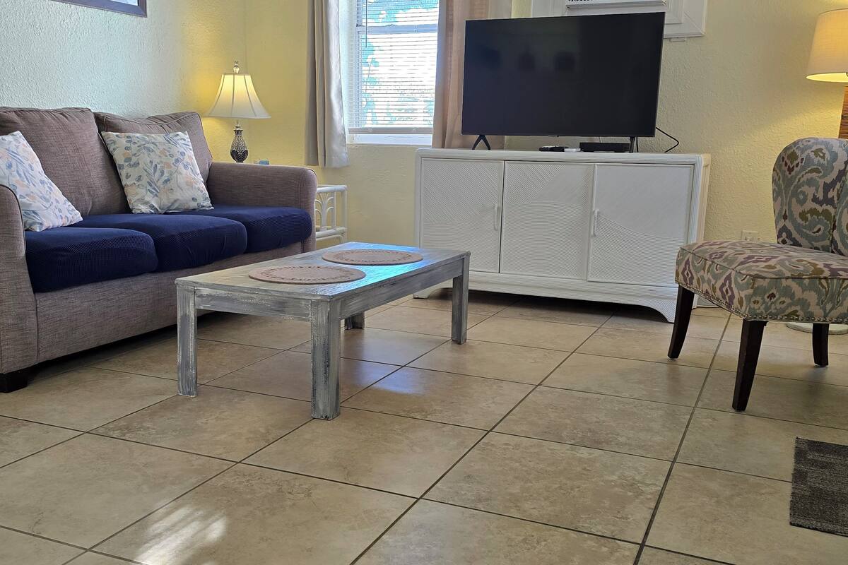 Una sala de estar con sofá, una mesa de centro, televisor y un sillón estampado.