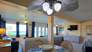 A hotel room with a balcony, a dining area with a table and chairs, a bed, a TV, and a ceiling fan. - Sea Scape Oceanfront Motel (Indialantic)