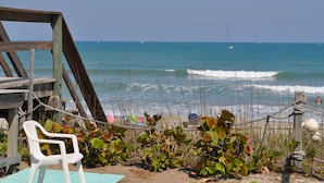 A beach with a wooden structure, a white plastic chair, and a rope fence. - Sea Scape Oceanfront Motel (Indialantic)