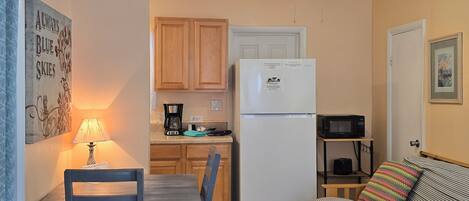 A compact kitchen with wooden cabinets, a white refrigerator, a microwave, and a dining area with a table and chairs.