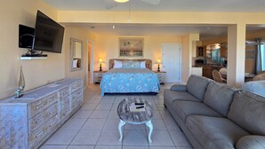 A bedroom with a bed, bedside lamps, a television, and a ceiling fan. - Sea Scape Oceanfront Motel (Indialantic)