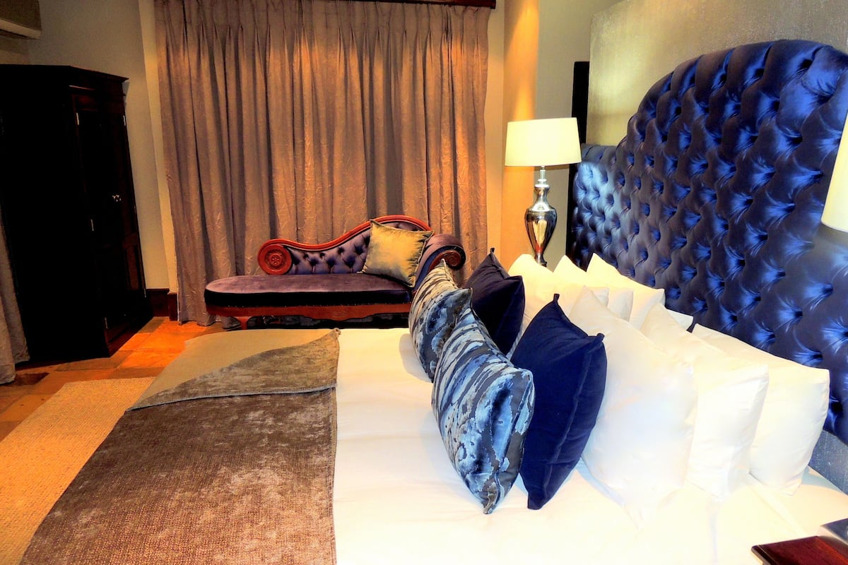 A hotel room with a large bed, a sofa, a lamp, and a curtain.
