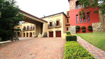 A courtyard with a brick pathway, a yellow building with red doors, and a red building with a balcony.