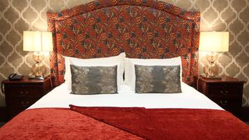 Un lit avec une couverture rouge, deux oreillers et une tête de lit à motifs. Il y a deux tables de chevet, chacune avec une lampe, et un téléphone sur l’une d’elles.
