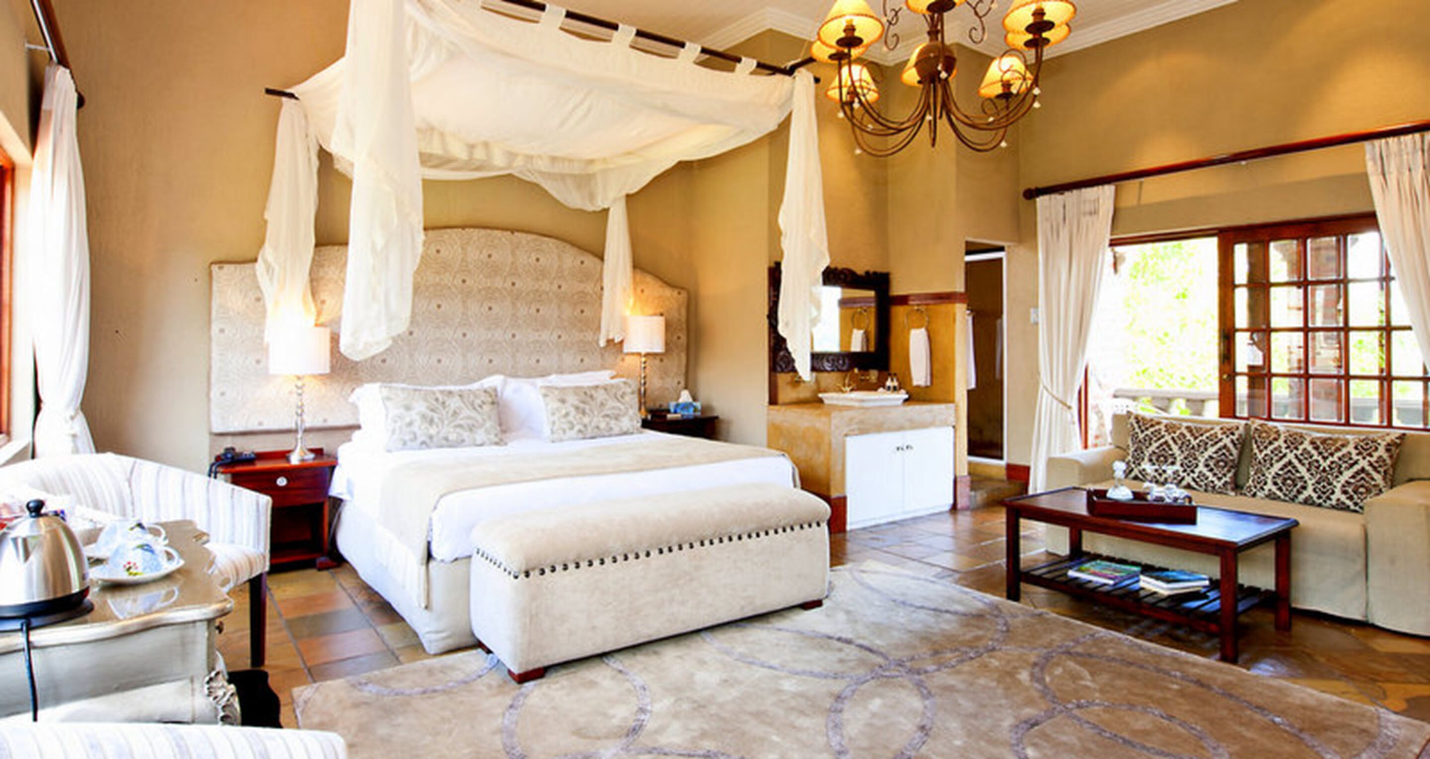A spacious bedroom with a large bed, a sitting area with a sofa, a coffee table, and a chandelier.