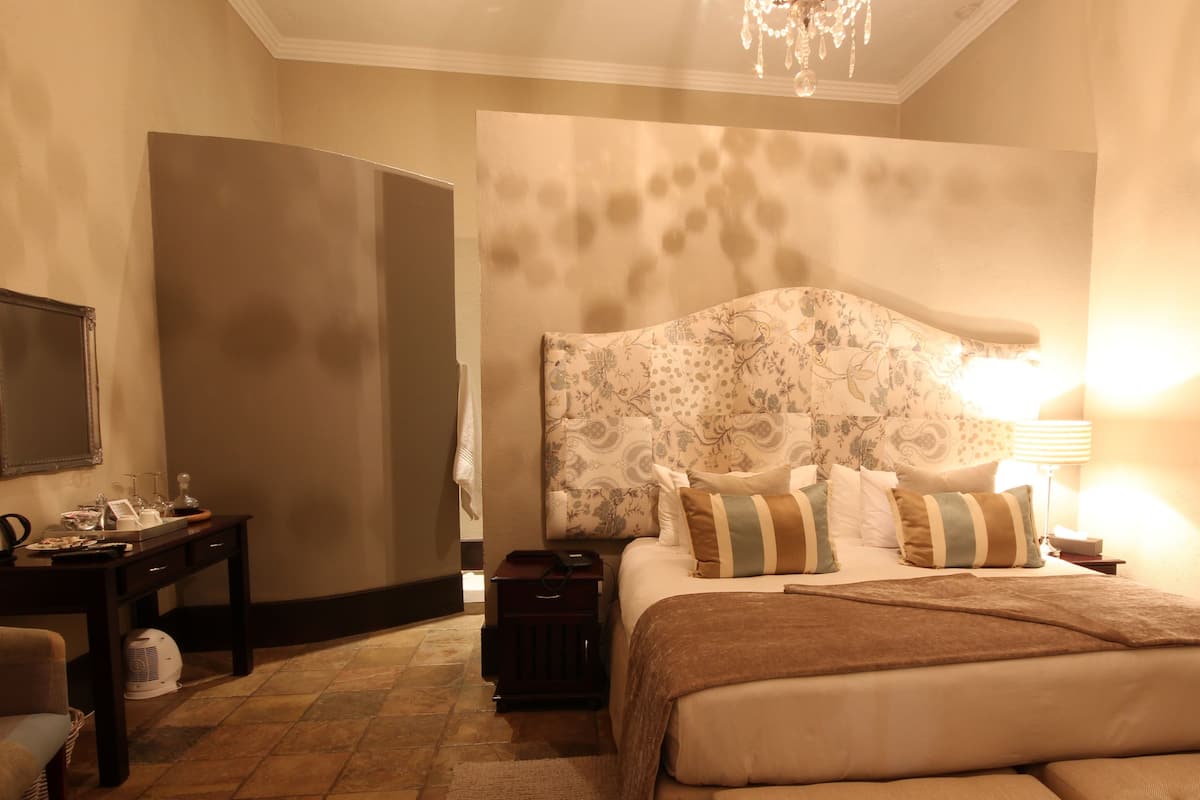 A hotel room with a large bed, a nightstand, a chair, a desk, and a chandelier.