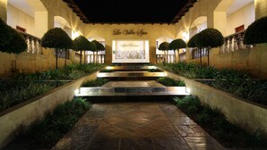 Entrada de hotel con un letrero que dice "La Villa Spa", un camino de piedra y jardines simétricos con setos podados.