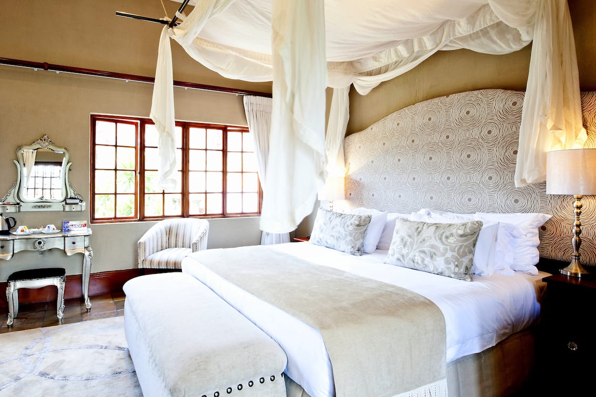 A bedroom with a canopy bed, a vanity with a mirror, and a window with curtains.