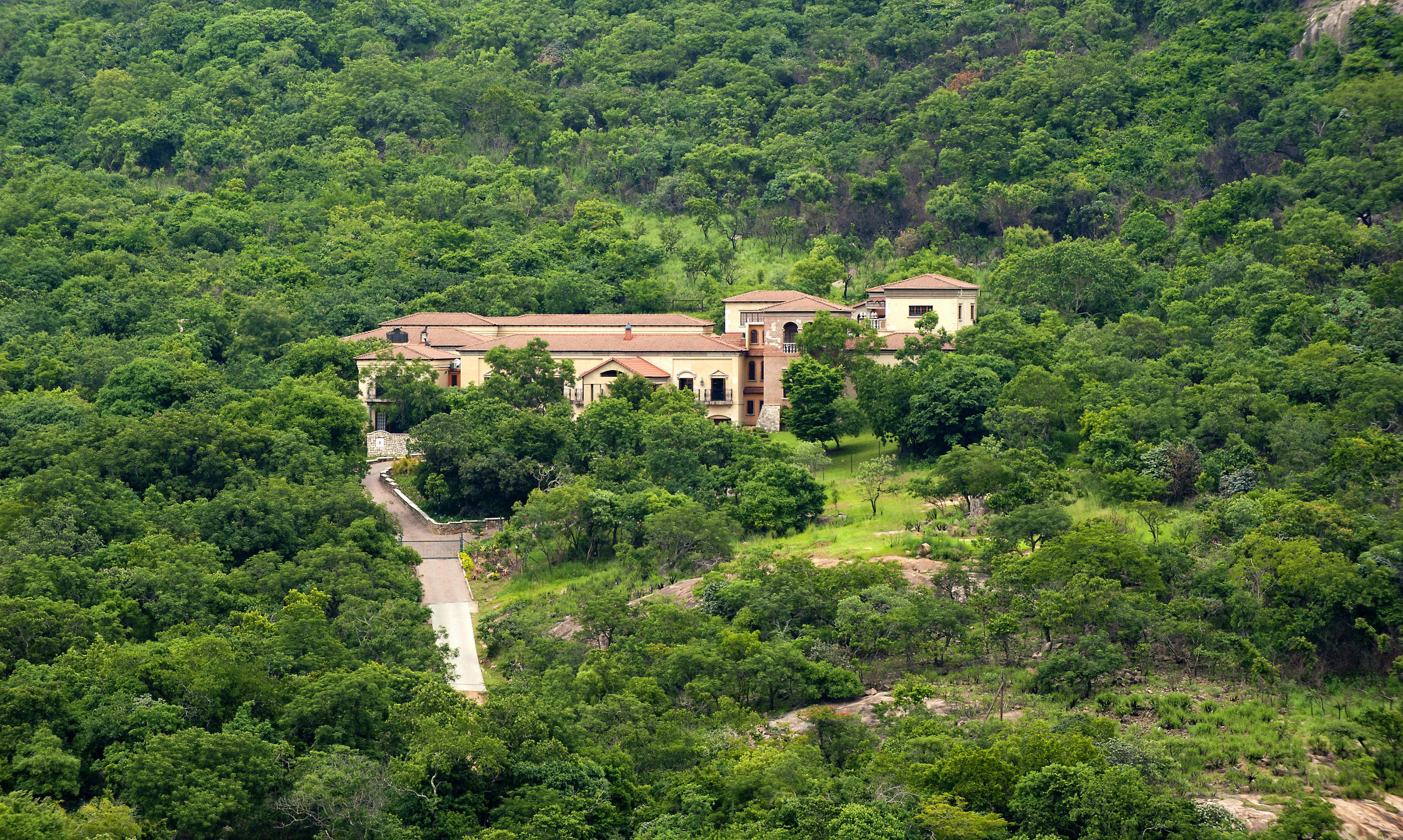 Un grand bâtiment à plusieurs étages, entouré d’une forêt dense, avec un chemin pavé menant à l’entrée.