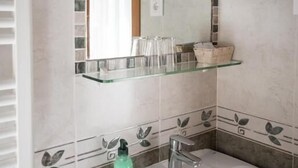 Un bagno con un lavandino bianco, uno specchio e uno scaffale in vetro sopra.