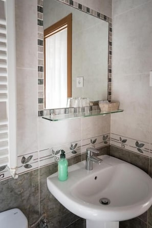 A bathroom with a white sink, a mirror, and a glass shelf above it. - San Antonio (Madrid)