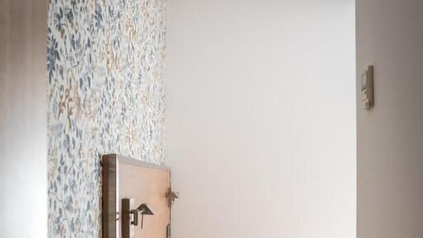 A bedroom with a wooden bedside table, a bed with a white duvet, a radiator, and a patterned wallpaper on the wall. - San Antonio (Madrid)