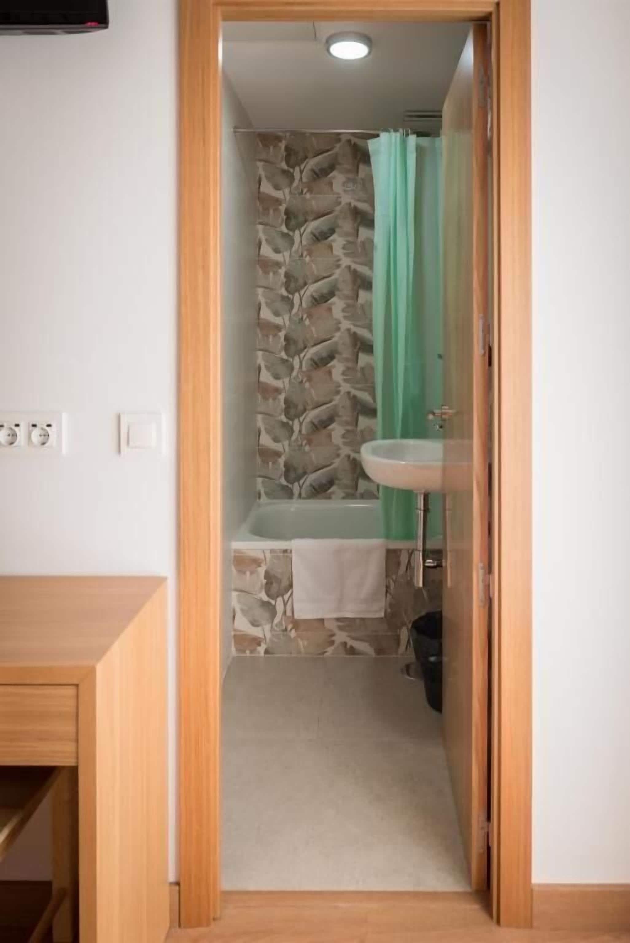 Een badkamer met een stenen muur, een badkuip, een wastafel en een groen douchegordijn.