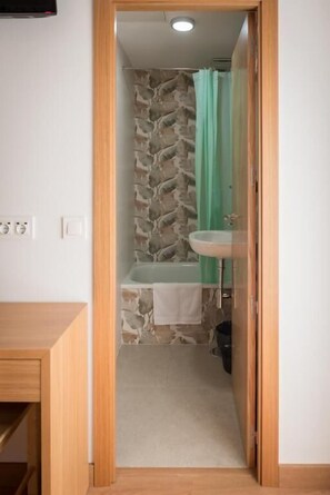 A bathroom with a stone wall, a bathtub, a sink, and a green shower curtain. - San Antonio (Madrid)