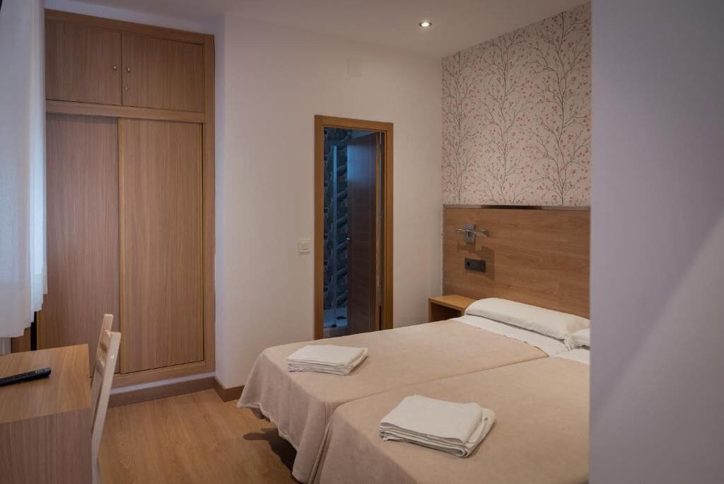 Un dormitorio con dos camas, un armario de madera, una mesita y una puerta que da a una escalera.