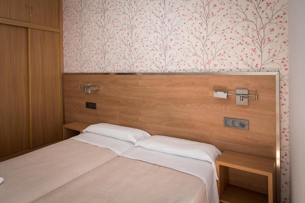 A bedroom with a wooden headboard, two beds, a nightstand, and a wardrobe.
