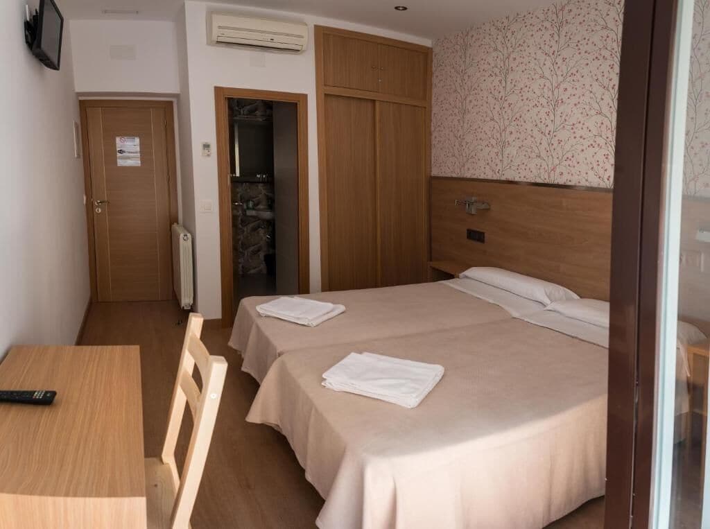 Una camera d'albergo con un letto, un armadio in legno, un termosifone e un tavolo con un telecomando.