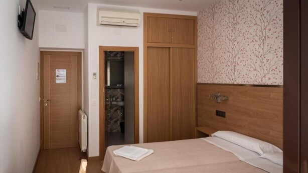 Una camera d'albergo con un letto, un armadio in legno, un termosifone, una televisione a parete e una porta con un cartello.