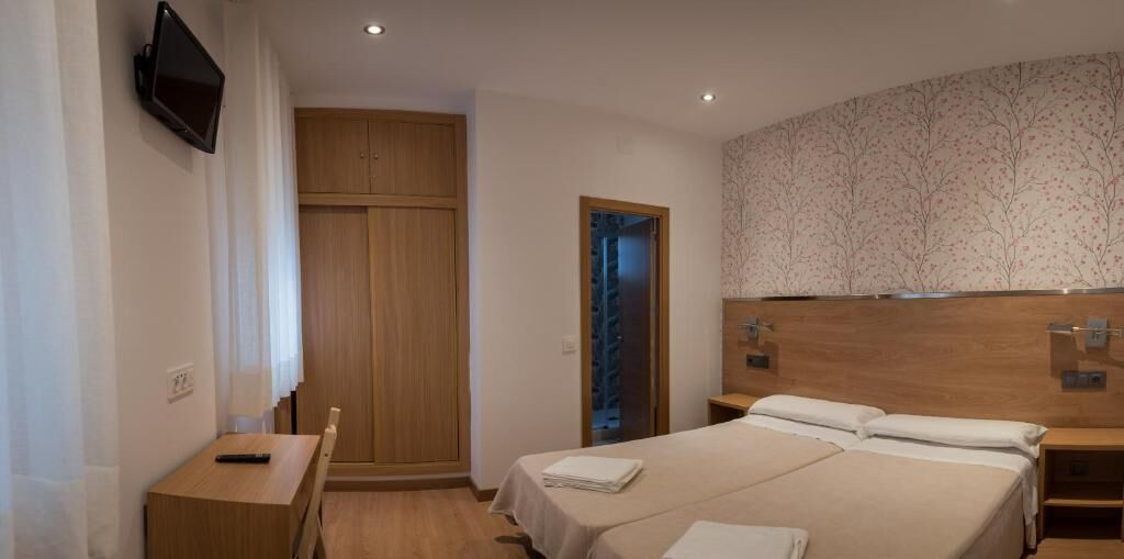A bedroom with a bed, bedside tables, a desk, a TV, a wardrobe, and a bathroom door.