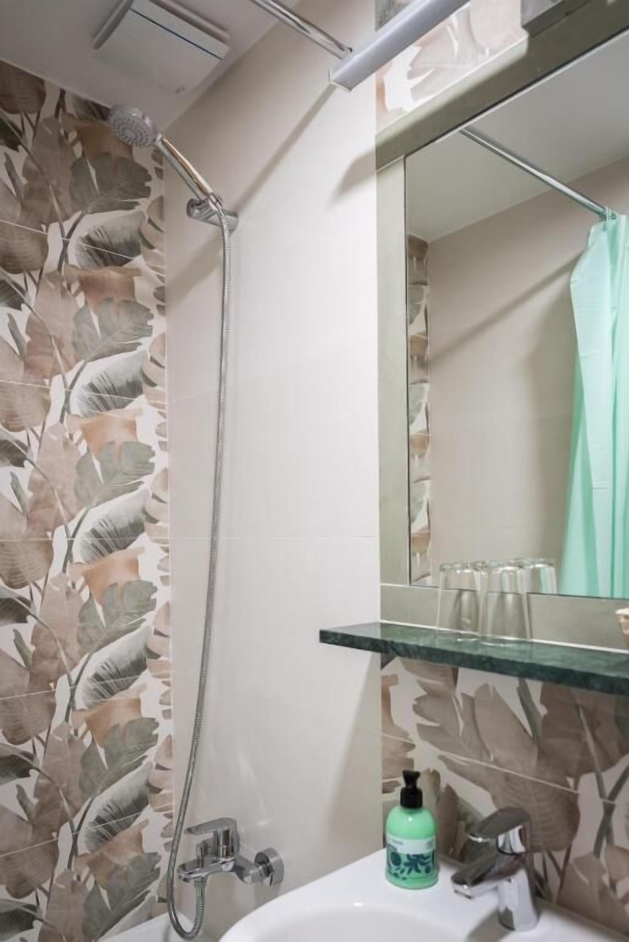 Een badkamer met een douche, een wastafel, een spiegel en een groene zeepfles.