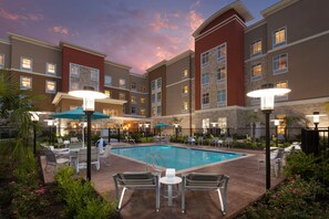 A hotel with a swimming pool, outdoor seating, and a sunset sky. - Homewood Suites by Hilton North Houston/Spring (Spring)