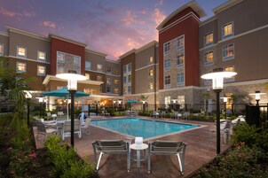 Un hotel con piscina, zona de estar exterior y cielo al atardecer.