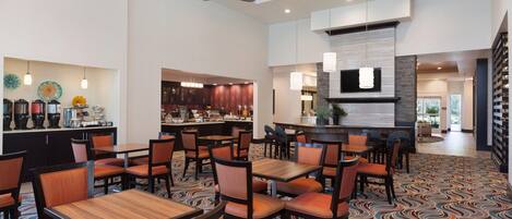 A hotel lobby with multiple seating areas, a bar, and a kitchen visible in the background.