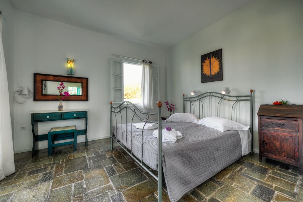 A bedroom with a metal bed frame, a wooden desk, a mirror, and a stone-patterned floor.