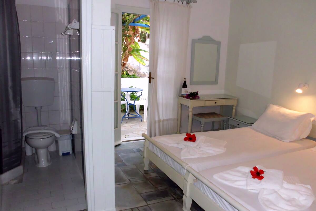A hotel room with a bed, a bathroom, and a small table with a bottle and flowers.